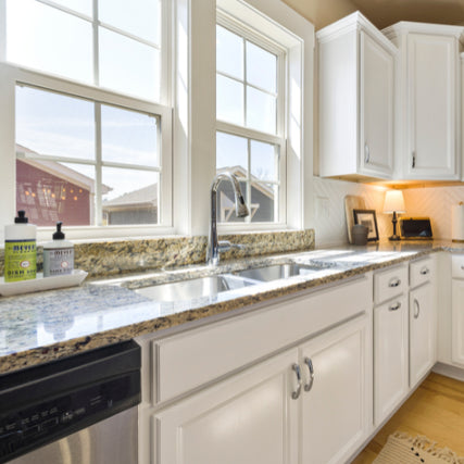 WindowsBright kitchen with white cabinets, granite countertops, and a double sink beneath large windows. Soap bottles and a small lamp create a cozy ambiance.