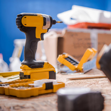 Power ToolsA yellow cordless drill stands on a wooden table surrounded by drill bits and boxes. The bright blue background conveys a busy workshop atmosphere.